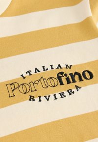 Geel en wit gestreepte stof met geborduurde teksten "Portofino" en "Italiaanse Rivièra" in het zwart. Zachte textuur, casual ontwerp.
