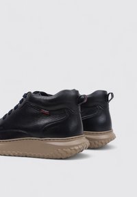Zapatillas altas de cuero negro con un acabado texturizado, suela de goma beige, cordones azules y lengüetas en el talón para ponerlas con facilidad.
