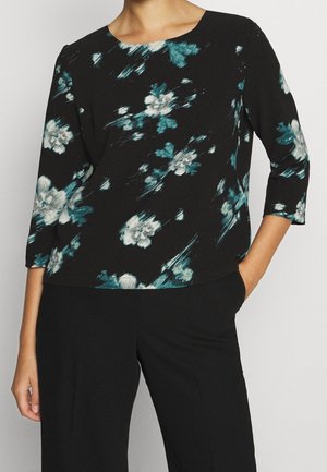 Blusa nera con motivo floreale in teallo e bianco, scollatura rotonda, maniche a tre quarti e vestibilità rilassata. Tessuto morbido e dalla texture particolare.