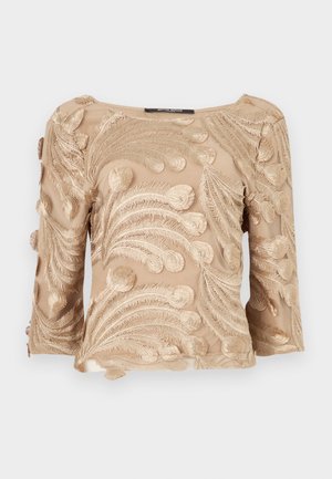 Beige gjennomsiktig bluse med intrikate broderte bregnelignende mønstre, med trekvart ermer og rett halsåpning.