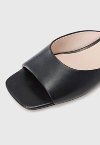 Μαύρο ανοιχτό πέδιλο κατασκευασμένο από δερμάτινη επιφάνεια με υφή, με φαρδιά λουρί μπροστά και σχεδιασμό με τετράγωνη μύτη.