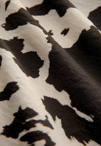 Black and white fabric with a cowhide pattern, smooth texture, and crisp design. The fabric drapes gracefully with visible folds.