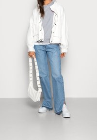 Chaqueta bomber blanca, sudadera gris, jeans de campana azul claro, zapatillas blancas y un bolso de hombro blanco con correa tachonada y forma redondeada.