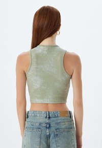 Top corto verde metallico con texture a coste e design senza maniche, abbinato a jeans in denim chiaro a vita alta.
