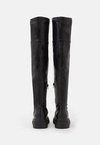 Czarne skórzane kozaki za kolano o gładkiej fakturze, z wewnętrznymi zamkami błyskawicznymi i grubą, masywną podeszwą. Pionowe szwy podkreślają design.