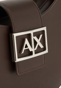 Καφέ δερμάτινη ζώνη με ασημένια ορθογώνια αγκράφα που φέρει ανάγλυφα τα γράμματα "AX" και το χαράγμα "Armani Exchange" στην κάθετη μπάρα.