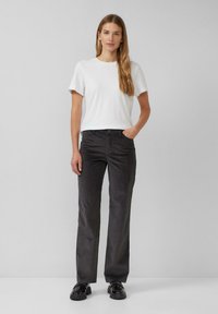 T-shirt blanc à manches courtes associé à un pantalon droit gris foncé, présentant un tissu texturé et un design simple. Des chaussures noires complètent le look.