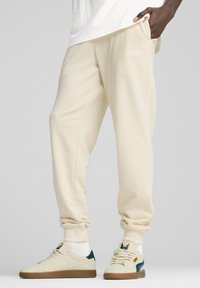 Beige sweatpants lavet af blødt stof, med en sidelomme og ribbede manchetter. Sat sammen med lette sneakers med grønne og farverige accenter.