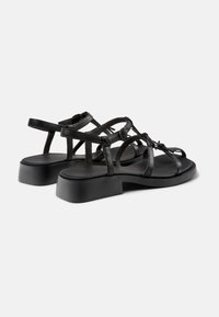 Black leather sandals with a low block heel, featuring crisscross straps, a toe loop, and an adjustable ankle strap. Smooth finish.