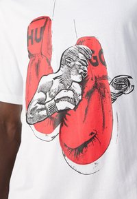 Boxer in Schwarzweiß-Skizze, der große rote Boxhandschuhe mit den Buchstaben "HU" und "GO" auf einem weißen Stoffhintergrund schlägt.
