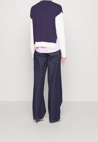 Mörkblå och vit färgblockerad kortad tröja över en rosa randig skjorta, matchad med vida mörkblå jeans och ljusa klackar.