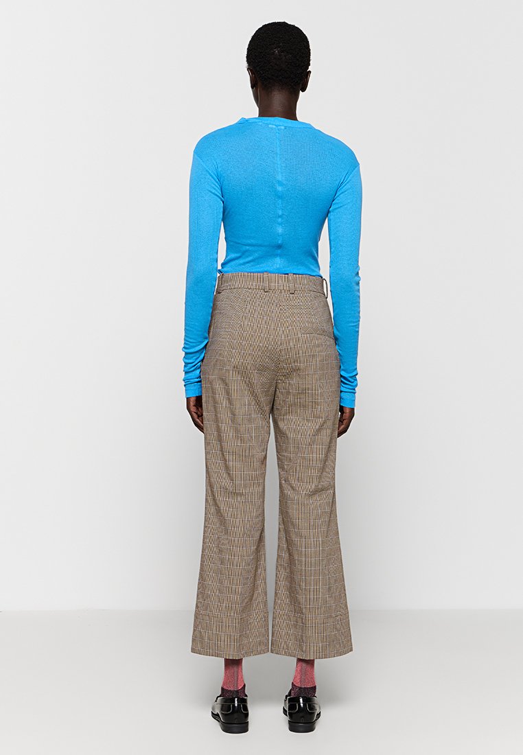Niebieska bluzka z długim rękawem połączona z wysokim w pasie, szerokim spodniami w kratę. Ubranie charakteryzuje się gładką teksturą oraz żywymi kolorami, kontrastującymi wzorami.