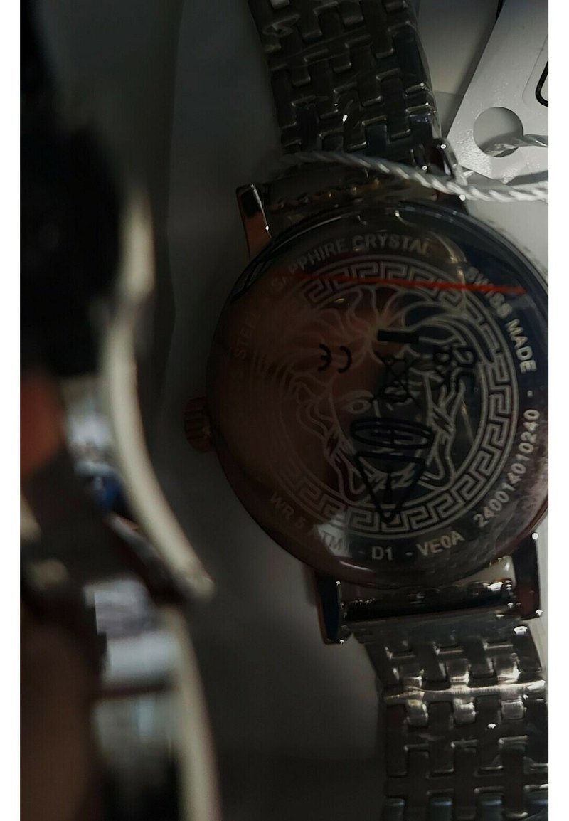 Orologio in acciaio inox argentato con cinturino decorato, quadrante in cristallo di zaffiro di forma rotonda e un design decorativo che presenta una testa stilizzata.