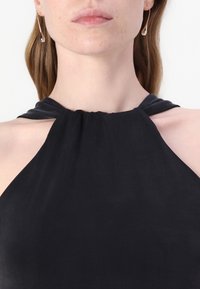 Crni top s halter izrezom i naboranim dekolteom, izrađen od glatkog materijala. Ima asimetrični kroj i minimalnu opremu.