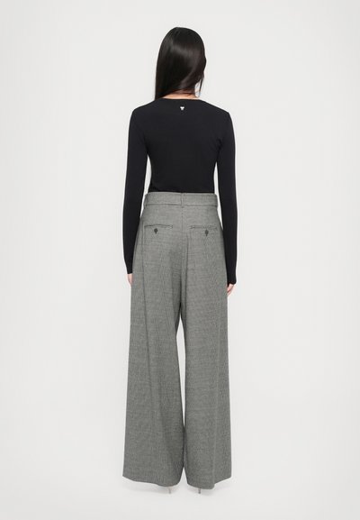 Haut noir à manches longues avec un col rond, associé à un pantalon large gris à carreaux taille haute avec poches arrière et boutons.