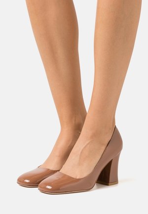 Talons en cuir verni marron avec un bout rond et un talon bloc. La surface est lisse et brillante, avec un design minimaliste.