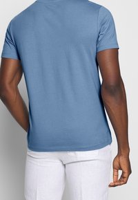 Camiseta de algodón azul de manga corta con cuello redondo, que presenta una textura suave y un corte relajado, con costuras visibles a lo largo del dobladillo.
