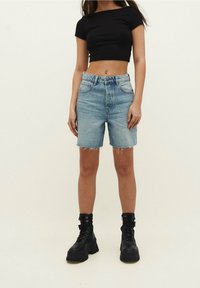 Camiseta negra cortada, pantalones cortos de mezclilla azul claro de cintura alta con bordes deshilachados, combinados con botas gruesas negras de cordones.