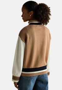 Kootud kampsun värviplokki disainiga, kus on pruun, valge ja tumesinine. Ribidega kaelus ja ääred koos triibulisete aktsentidega. Mugav lõige.