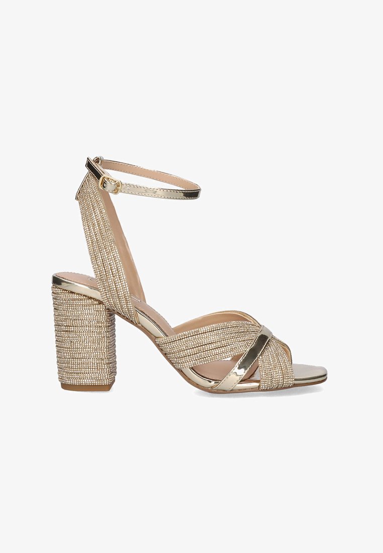 Sandalias de tacón alto doradas con un diseño trenzado texturizado y una correa en el tobillo, que presentan un tacón grueso texturizado y acentos metálicos.