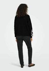 Zwarte gebreide trui met brede mouwen, versierd met een wit patroon, gecombineerd met zwarte rechte jeans en platte schoenen.