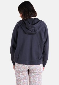 Haut à capuche gris foncé avec un cordon de serrage, des poignets et un bas côtelés. Logo visible sur l'épaule et tissu doux et texturé.