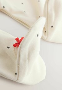 Knæhøje hvide sokker med sorte hjerte mønstre, prydet med en rød sløjfe. Blødt materiale, ribstrikkede manchetter og foldede toppe for ekstra komfort.