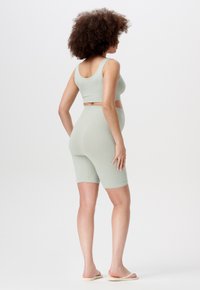 Lichtgroene geribde activewearset bestaande uit een fitting crop top en shorts tot halverwege de dij, met nadruk op een gladde textuur en een minimaal design.