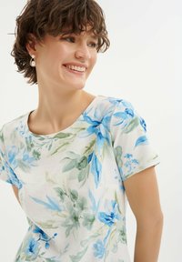 Kwiatowa bluzka z krótkim rękawem w niebieskie i zielone wzory akwarelowe na jasnym tle, wykonana z miękkiego, przewiewnego materiału.