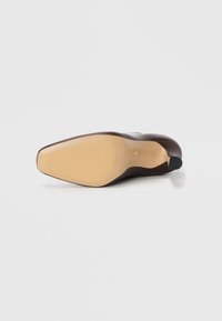 Semelle de chaussure en cuir marron avec une finition lisse, équipée d'une semelle extérieure en caoutchouc beige et d'un capuchon de talon noir, conçue avec une forme pointue.