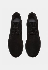 Stivaletti da uomo in suede nero, alla caviglia, con tre fori, punte tonde e lacci neri, mostrati dall'alto su uno sfondo bianco.