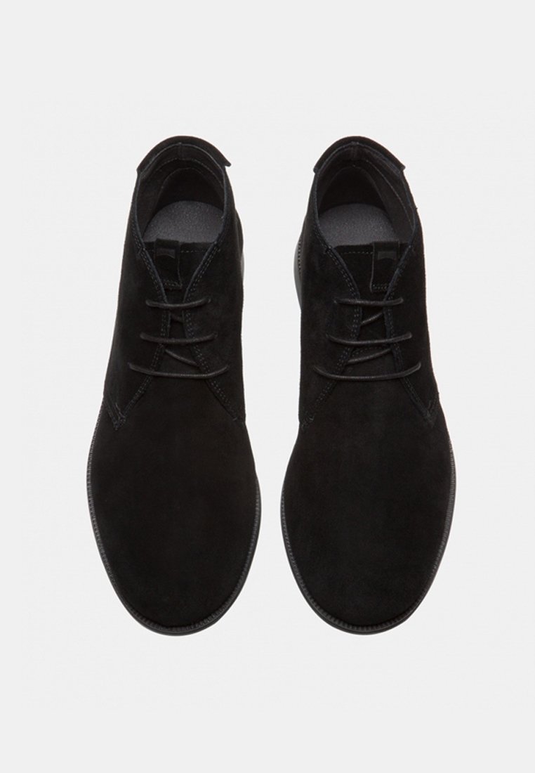 Sorte ruskinds herreankelstøvler med tre snørhuller, runde tæer og sorte snøre, vist ovenfra på en hvid baggrund.