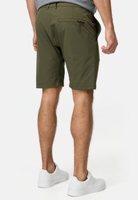 Shorts vert olive au design simple, dotés de poches latérales et d'une poche zippée à l'arrière. Portés avec des baskets blanches.