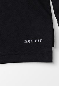 Musta Dri-FIT urheilu paita, jossa on lyhyet hihat ja hienovarainen rakenne, sekä valkoinen "DRI-FIT" printti helman läheisyydessä.
