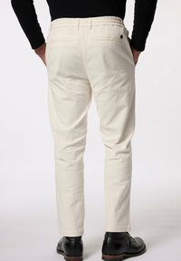 Světlé béžové kalhoty s elastickým pasem, slim fit, dvě zadní kapsy a hladká textura. Nosené s černými koženými botami.