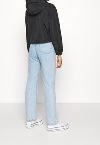 Svart kort jacka med huva, kombinerad med ljusblå raka jeans och vita sneakers. Slät tygkvalitet och avslappnad passform.