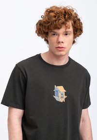 Zwart T-shirt met korte mouwen van katoen, met een kleurrijke vogelhuisgrafiek op de voorkant. Eenvoudig ontwerp met een ronde hals.
