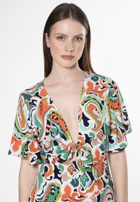 Vestito multicolore con scollatura a V profonda e maniche a a battito corte. Il tessuto presenta un bold, un motivo paisley vorticoso con accenti arancioni, verdi e blu navy.