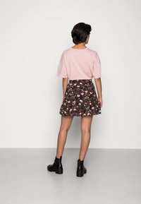 Chemise rose pâle à manches courtes associée à une jupe noire à motifs floraux avec un ourlet volanté. Bottines noires complètent la tenue.