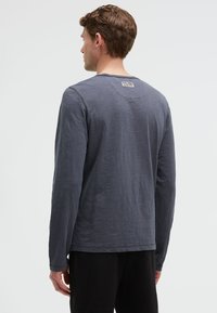 Langärmliges Shirt in Dunkelgrau, aus strukturiertem Stoff. Verfügt über einen Rundhalsausschnitt und ein kleines Etikett auf der Rückseite, mit lässigem Schnitt und minimalistischem Design.