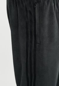 Ciemnoszare spodnie dresowe z trzema pionowymi czarnymi paskami i kieszenią na zamek po bokach.