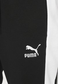 Melni sporta bikses ar baltām sānu strīpām, uz kreisā augšstilba ir balts izšūts Puma logo. Kokvilnas sajaukums, gluda tekstūra.