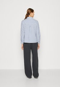 Camicia a righe blu e bianca con maniche lunghe, abbinata a pantaloni grigi scuri e morbidi. Design semplice, senza motivi o accenti visibili.