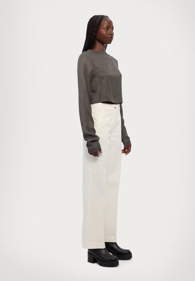 Top de manga larga a cuadros gris cortado, combinado con pantalones de pierna ancha blancos y botas de tobillo de plataforma negras, mostrado sobre un fondo neutro.