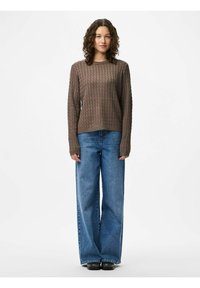 Maglione marrone lavorato a maglia con un motivo a rombi testurizzato, abbinato a jeans in denim blu a gamba larga. Maniche lunghe e scollatura a girocollo.