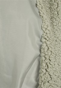 Mykt beige fleece-stoff med krøllete tekstur ved siden av glatt lys grått stoff, som viser kontrast i materialer og teksturer.