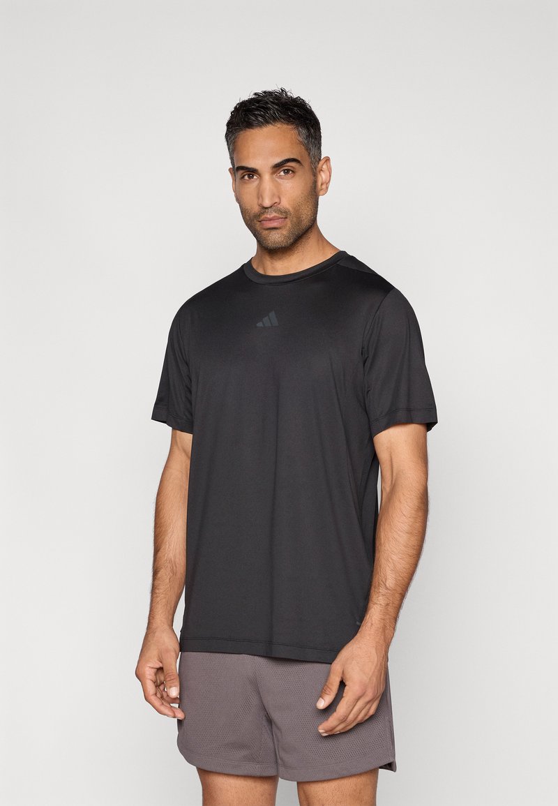 Μαύρο αθλητικό t-shirt με κοντά μανίκια, με αντανακλαστικό λογότυπο στο στήθος. Συνδυάζεται με ανοιχτό γκρι σορτς, με απαλή υφή υφάσματος.