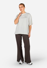 Gaiši pelēks liela izmēra t-krekliņš ar īsām piedurknēm, kura priekšpusē ir neliels logo. Apvienots ar tumši brūniem platiem biksēm ar sānu šķēlēm un baltiem sporta apaviem.