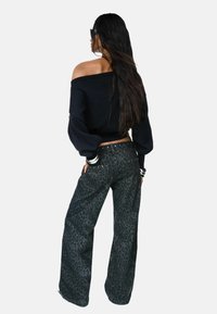 Un pull noir décolleté associé à un jean en denim foncé avec des jambes larges, comportant un subtil imprimé léopard et des détails cloutés sur les poches.
