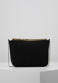 Sort stofhåndtaske med en tekstureret guldfarvet perledekoration øverst, med en sølvkæde som rem og en struktureret rektangulær form.